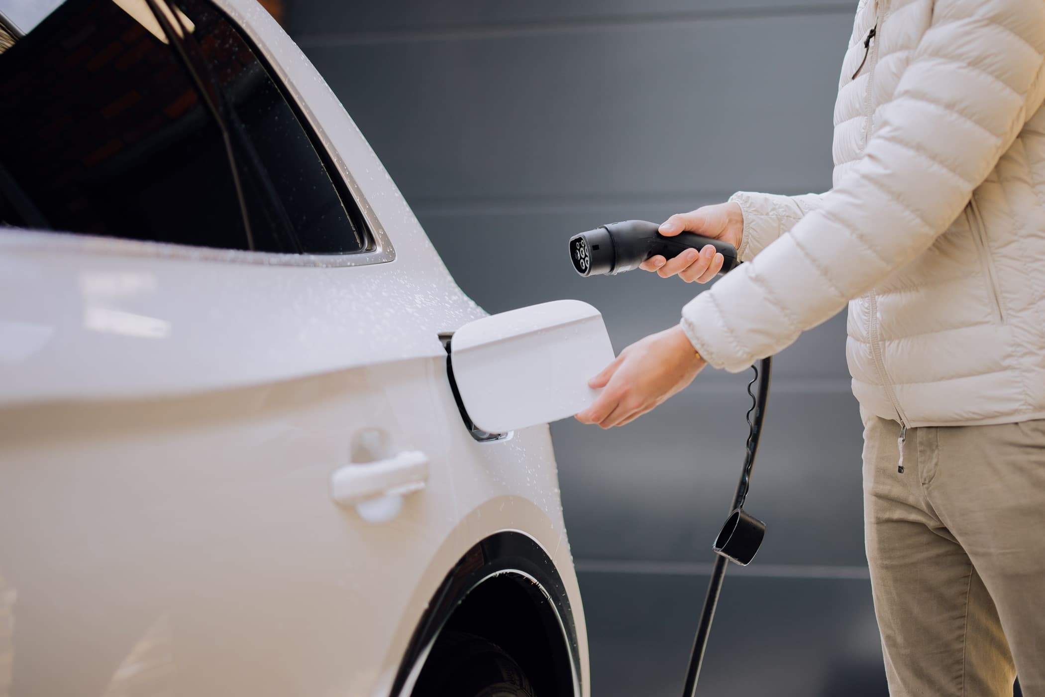 Iemand steekt de laadkabel in een elektrische auto op de oprit