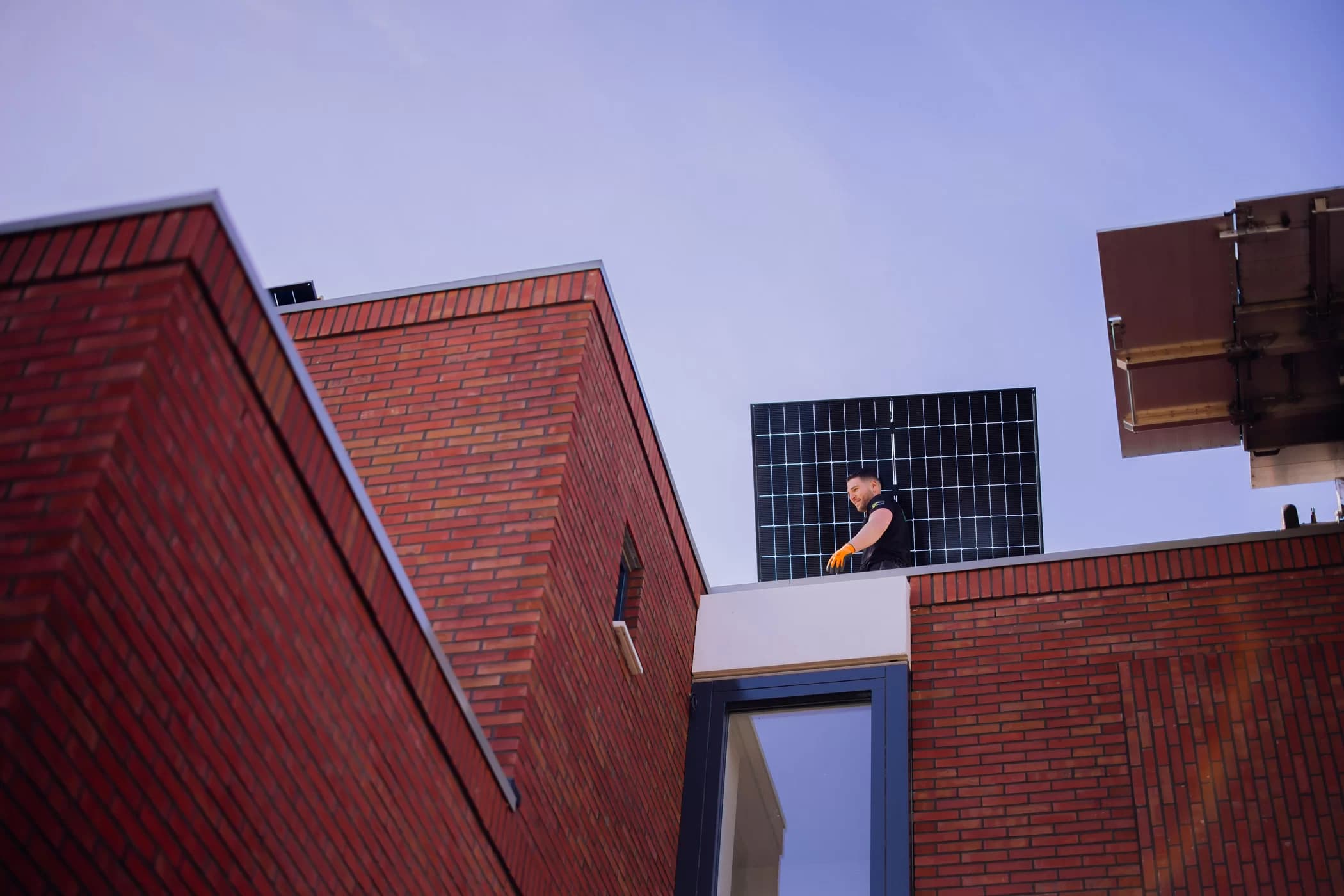 Monteur tilt een zonnepaneel over de dakrand van een woning